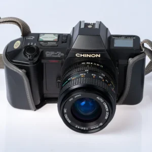 Chinon CP-7m -filmikamera mustana, kiinnitettynä Auto Chinon Zoom 35-70mm objektiivi ja kaulahihna
